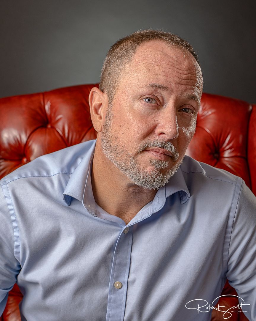 Portrait in red leather chair wearing light blue button-down shirt.