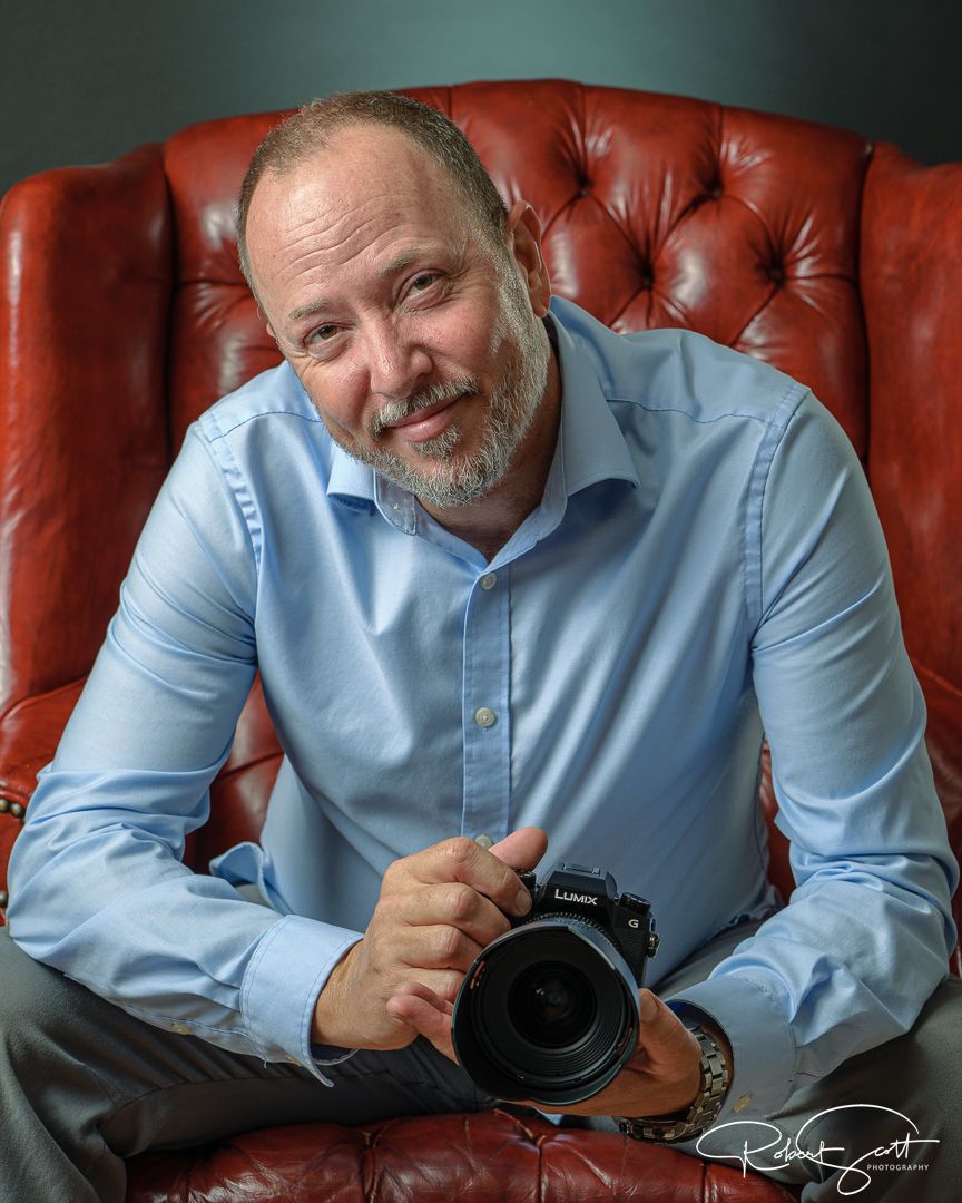 Photographer relaxes in red leather chair while holding professional camera.