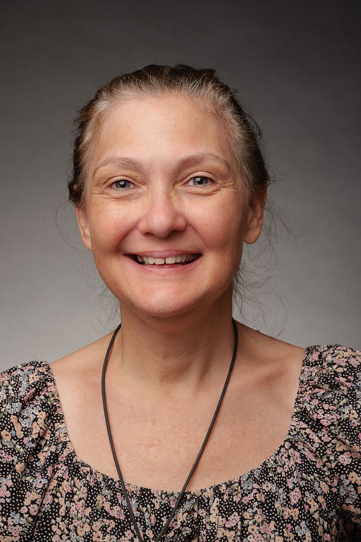 Portrait of a person in floral top with pulled back hair against gray background.