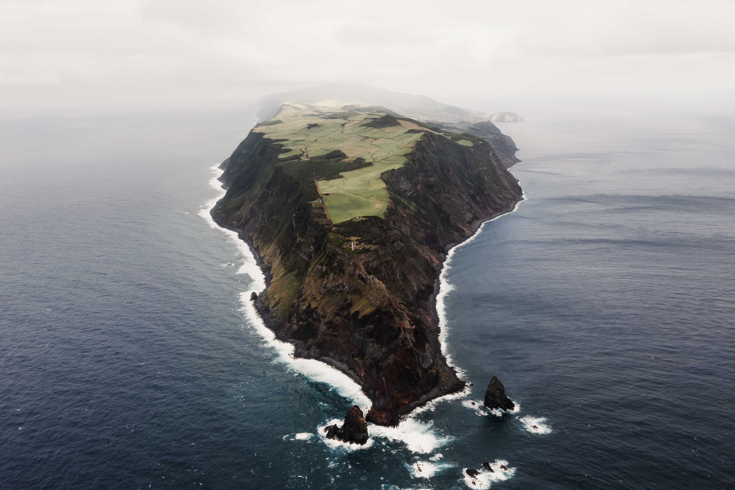 Bird's eye view of a triangular-shaped island peninsula surrounded by crashing waves.