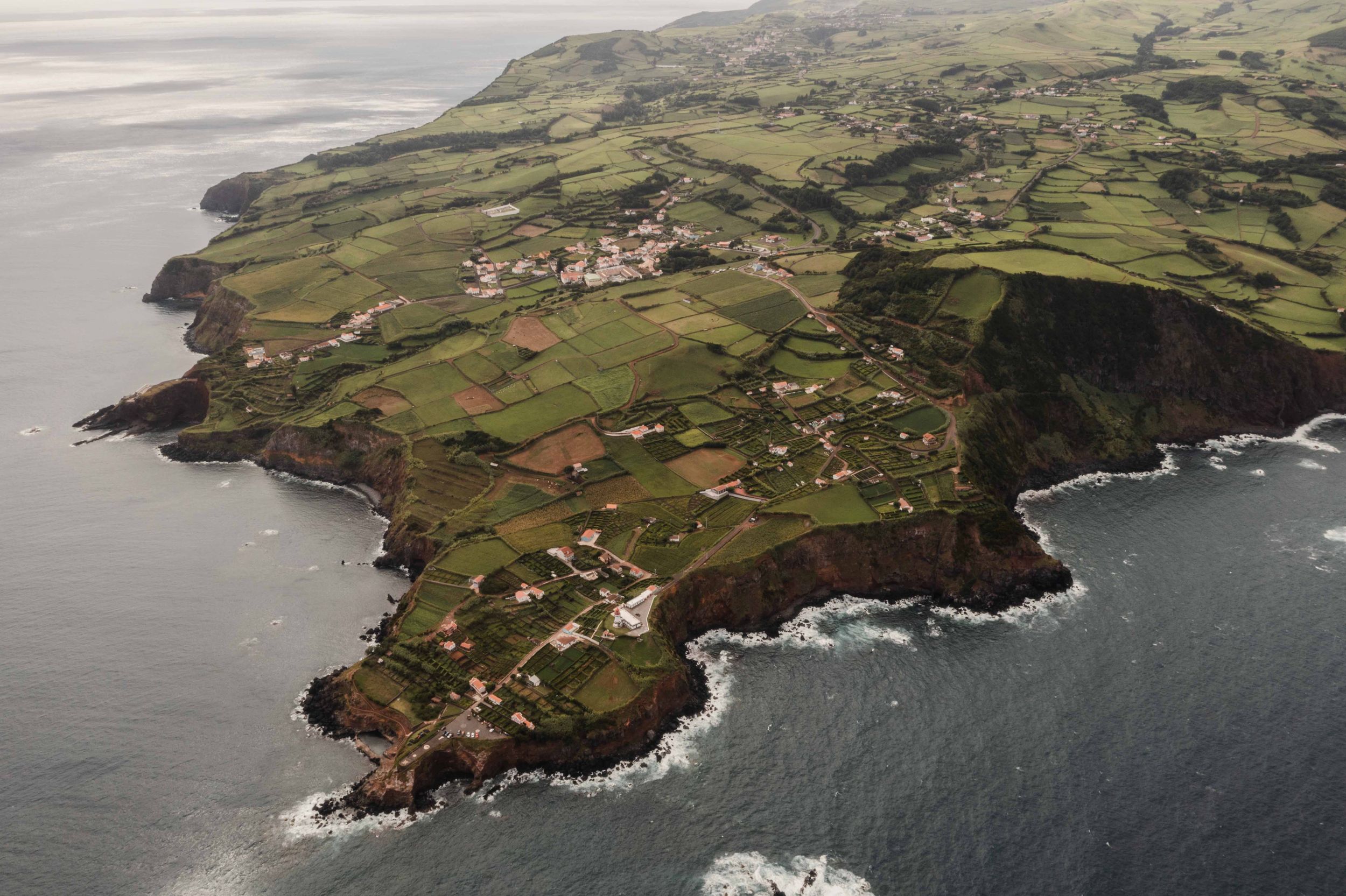 Aerial view of a rugged coastal peninsula with scattered buildings and farmland along dramatic cliffs.