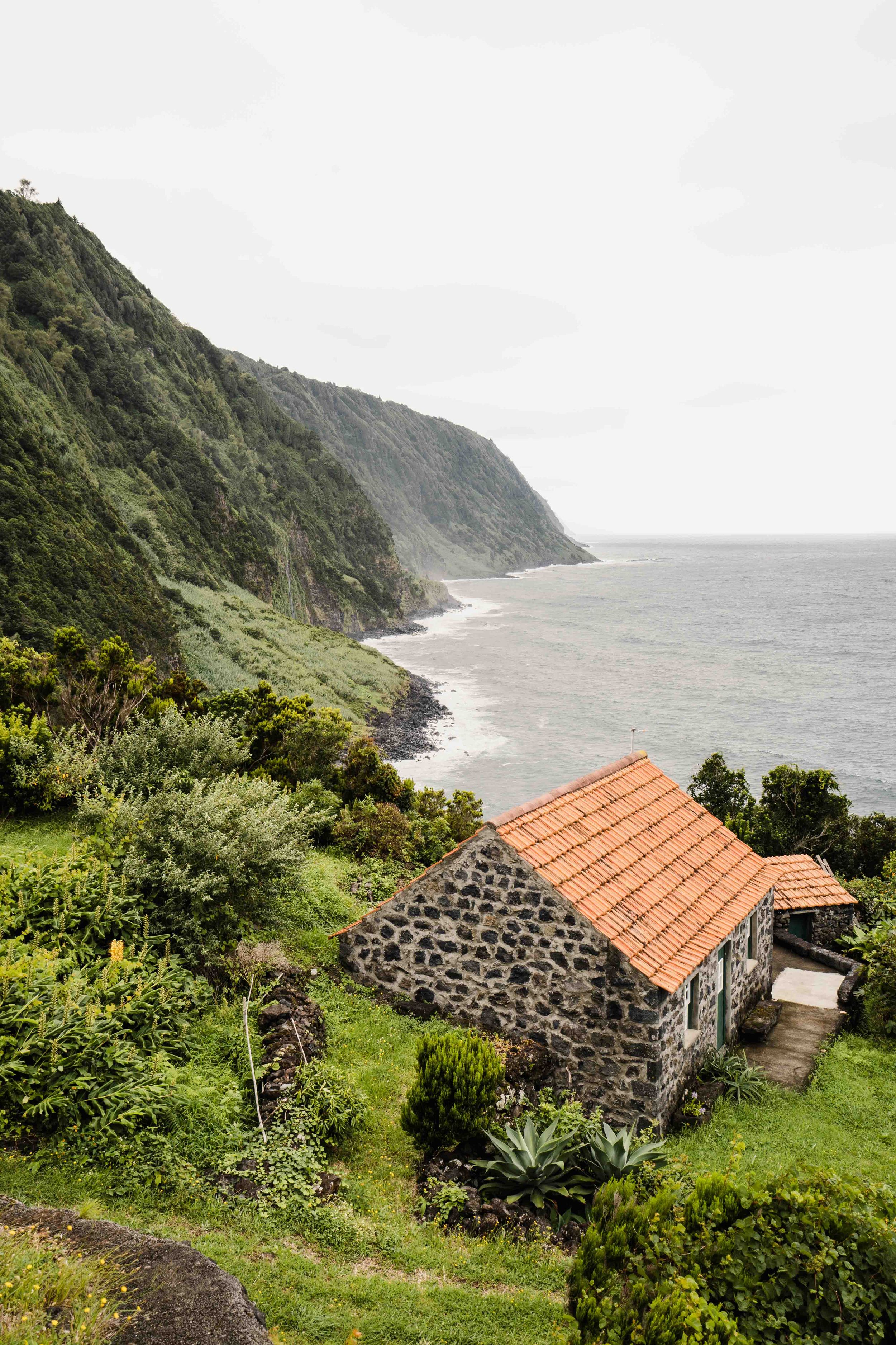 Stone cottage with terracotta roof overlooking steep coastal cliffs and the ocean.