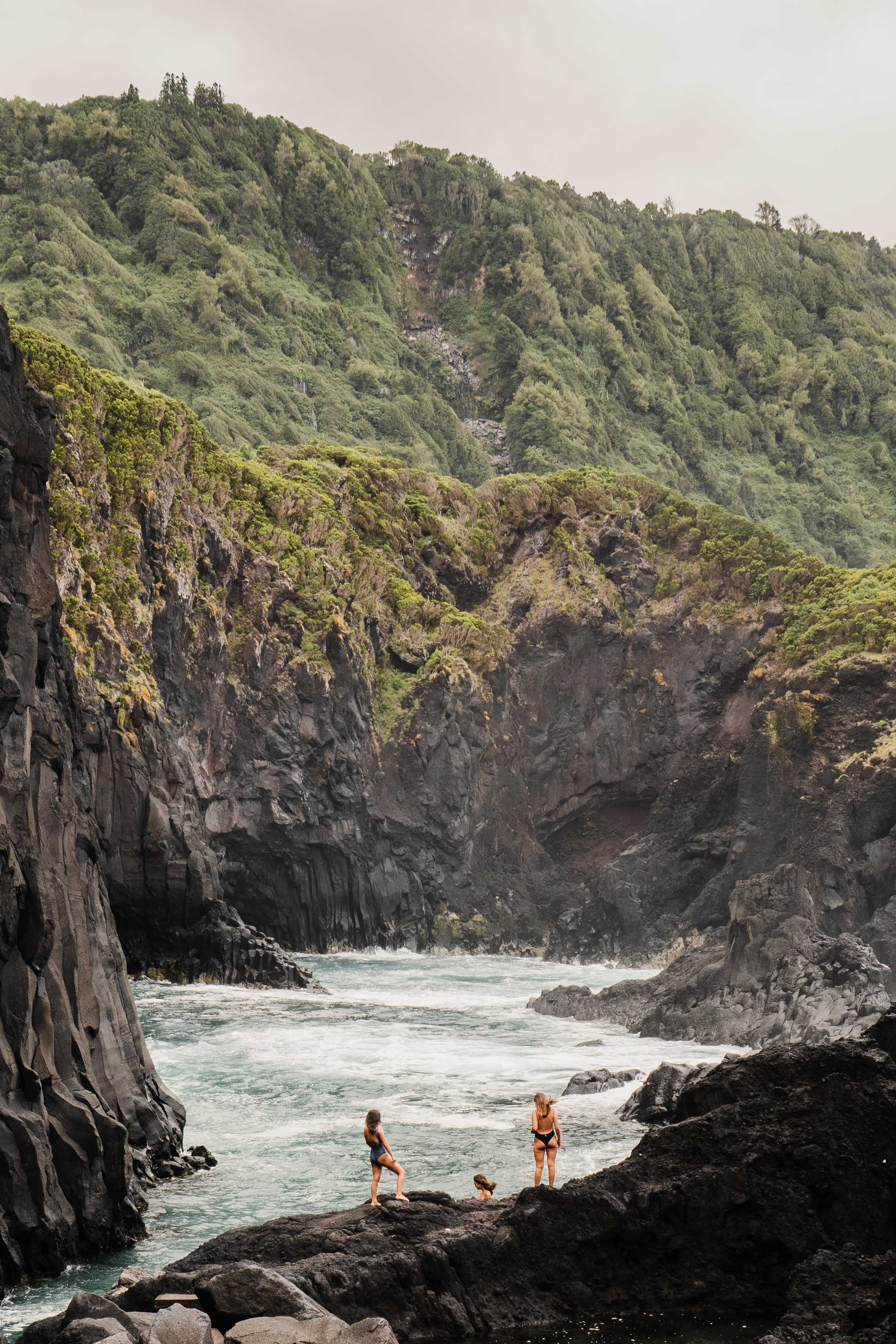 Dramatic rocky cove with volcanic cliffs and crashing waves along a rugged coastline.