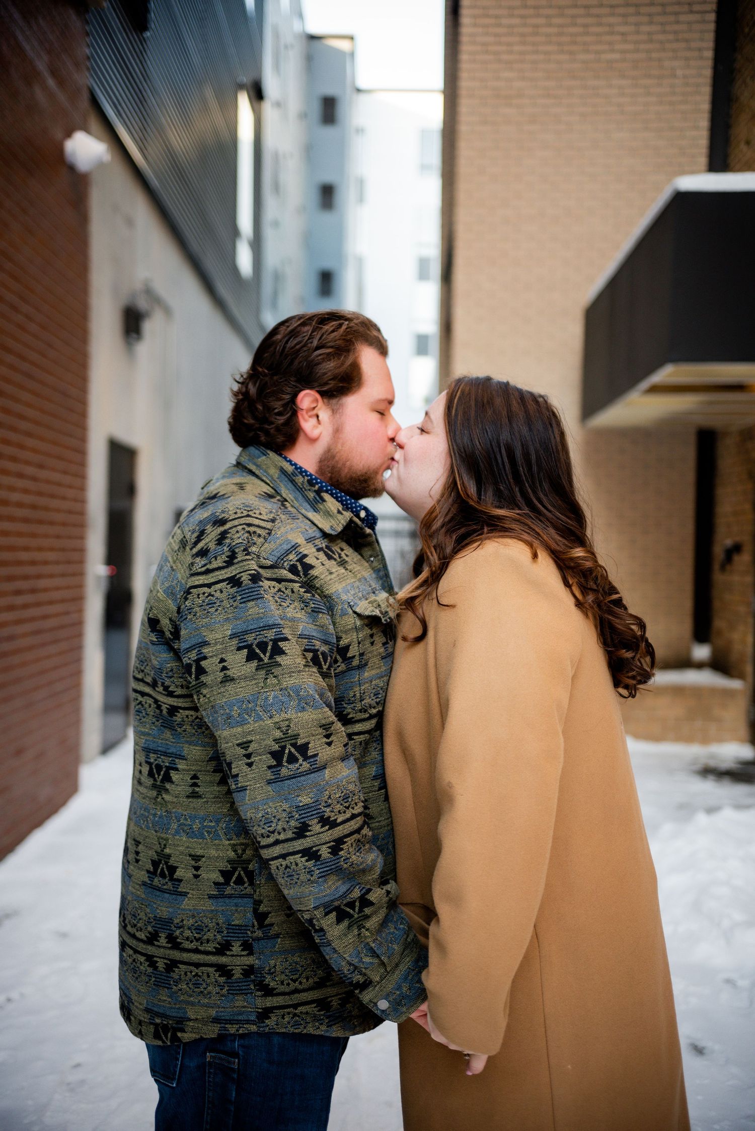 A romantic winter scene showing a couple sharing intimate moments against a snowy brick wall backdrop.