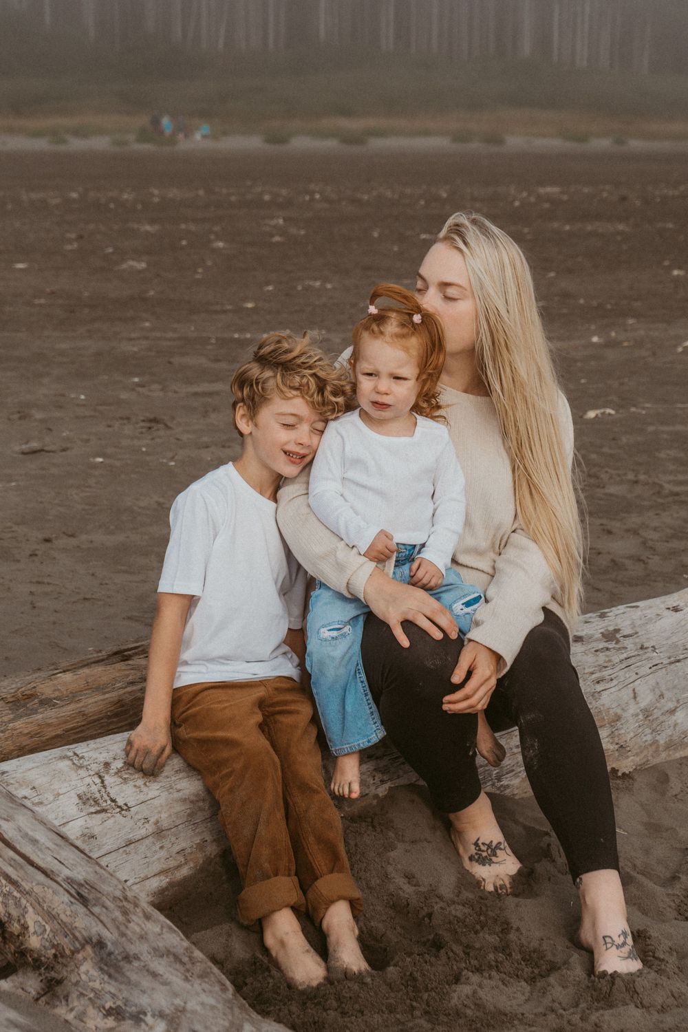 Family sharing intimate moment on driftwood at misty beach.