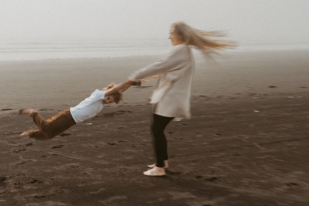 Child being swung playfully in circles on a foggy beach.