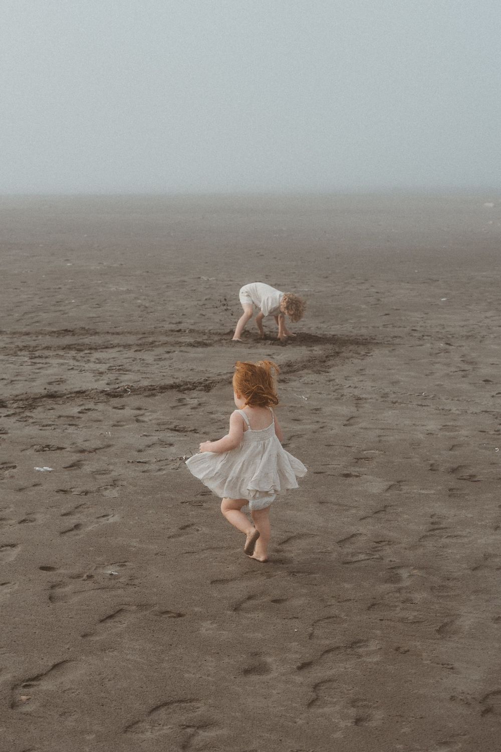 Children playing and twirling on a misty beach.