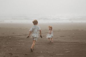 Two children running barefoot on misty beach.