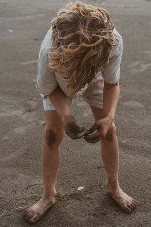 Person with sandy bare feet bending down to touch beach sand.