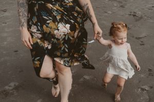Parent and child walking hand in hand on beach in casual outfits.