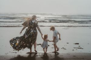 Family moment captured on misty beach with flowing dress in wind.