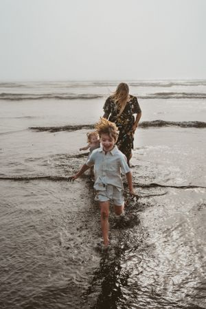 Family playing together in shallow ocean waves on a misty beach.