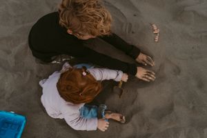 Two people lying on sandy beach playing together on an overcast day.