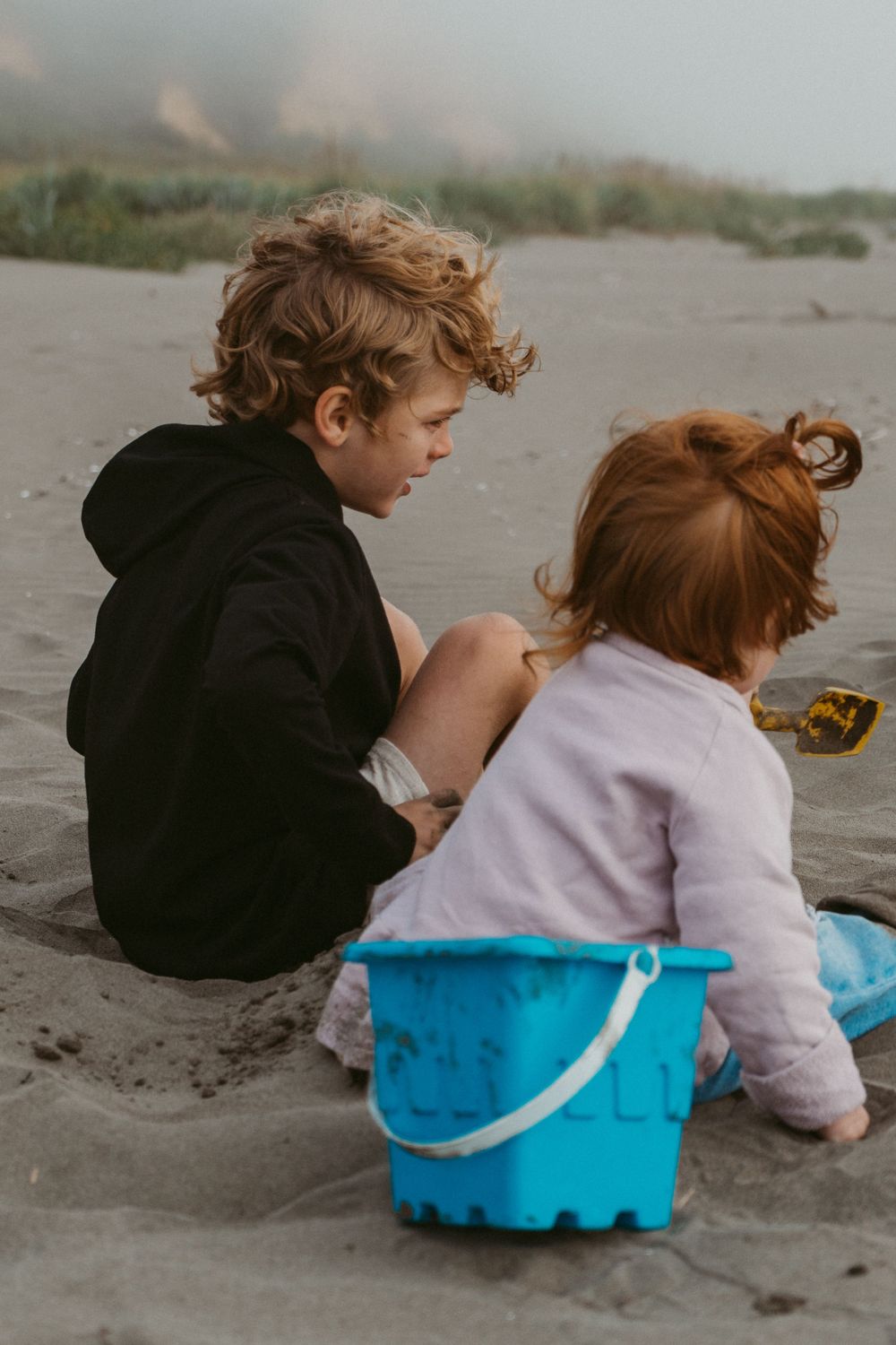 Children playing in the sand with a blue bucket on a misty beach.
