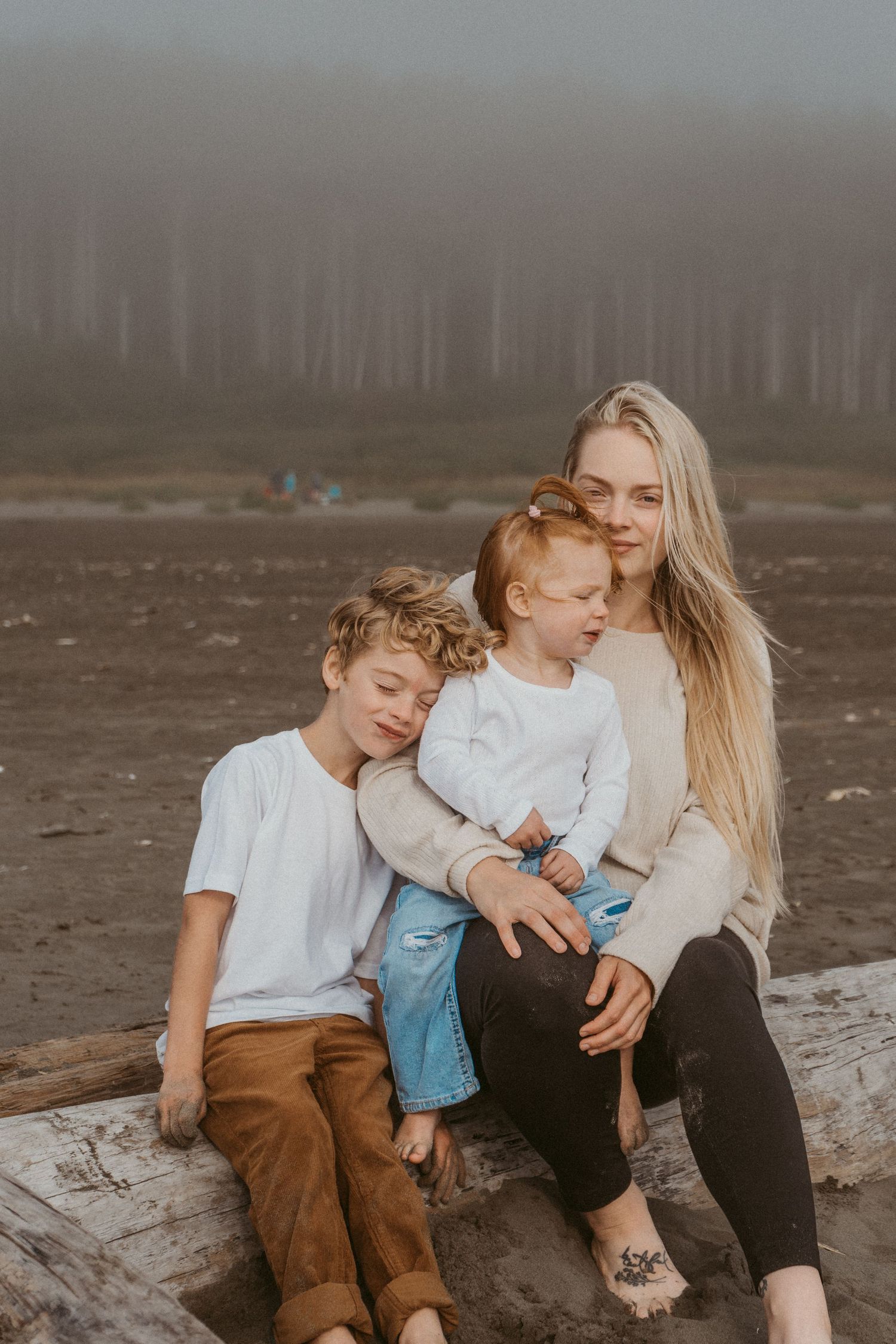 Intimate family moment captured on a driftwood log at a misty beach.