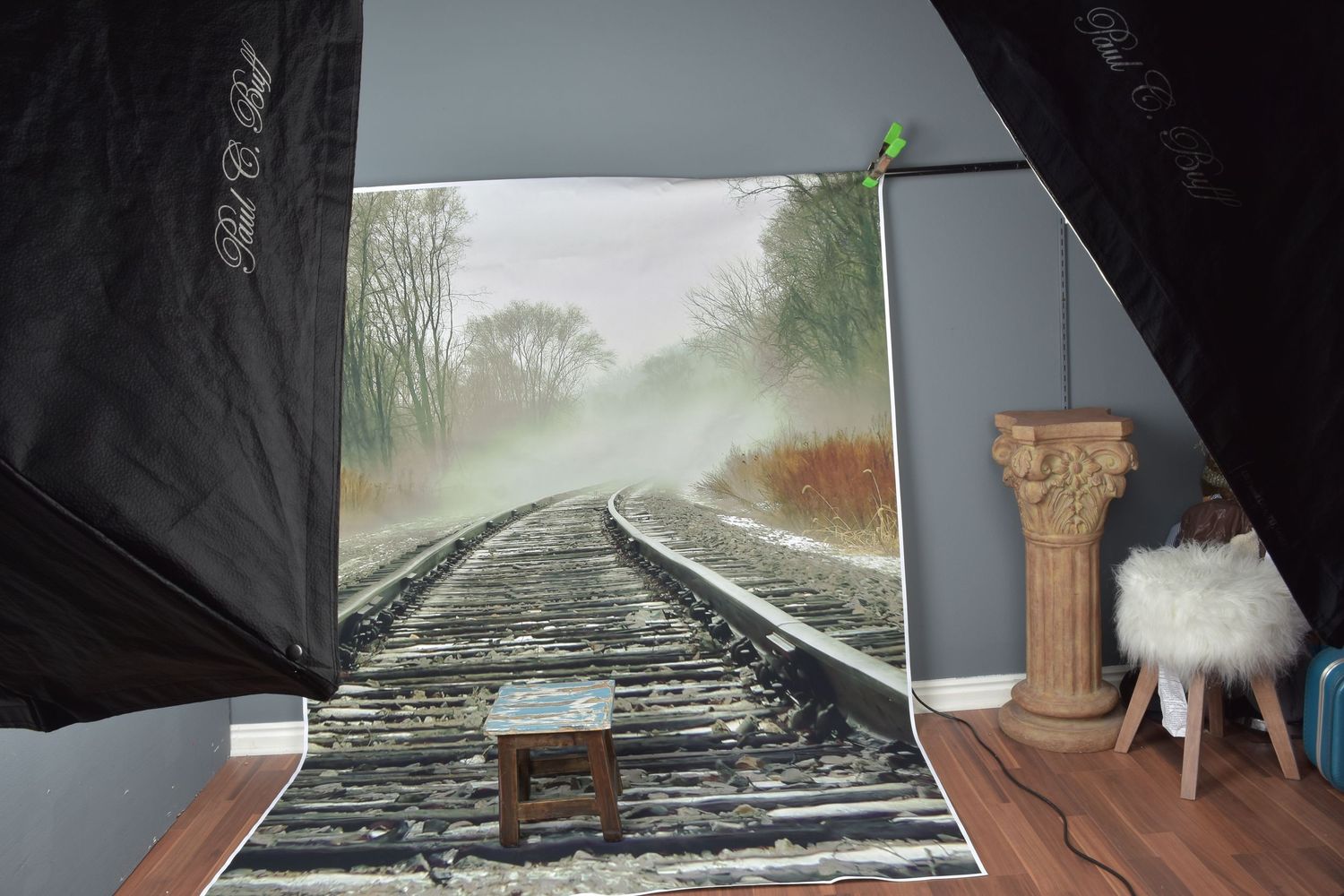 Photography studio setup with a railroad track backdrop, softbox lights, and decorative column prop on gray painted floor.