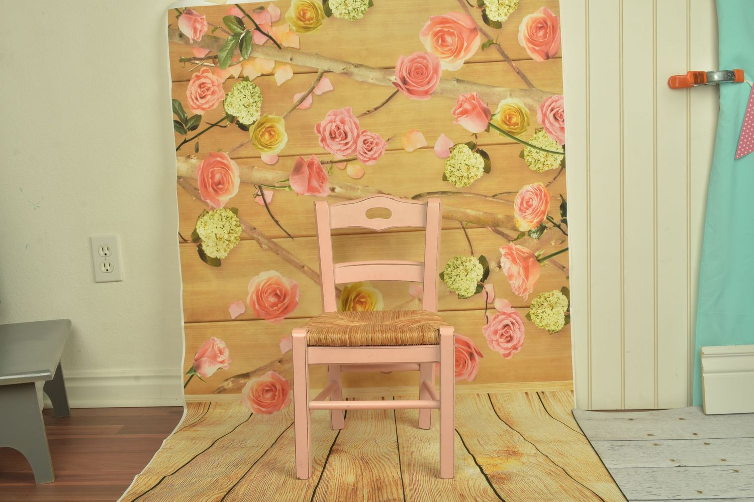 Pink child's chair against a wooden backdrop decorated with pink and green paper flowers for a photo shoot.