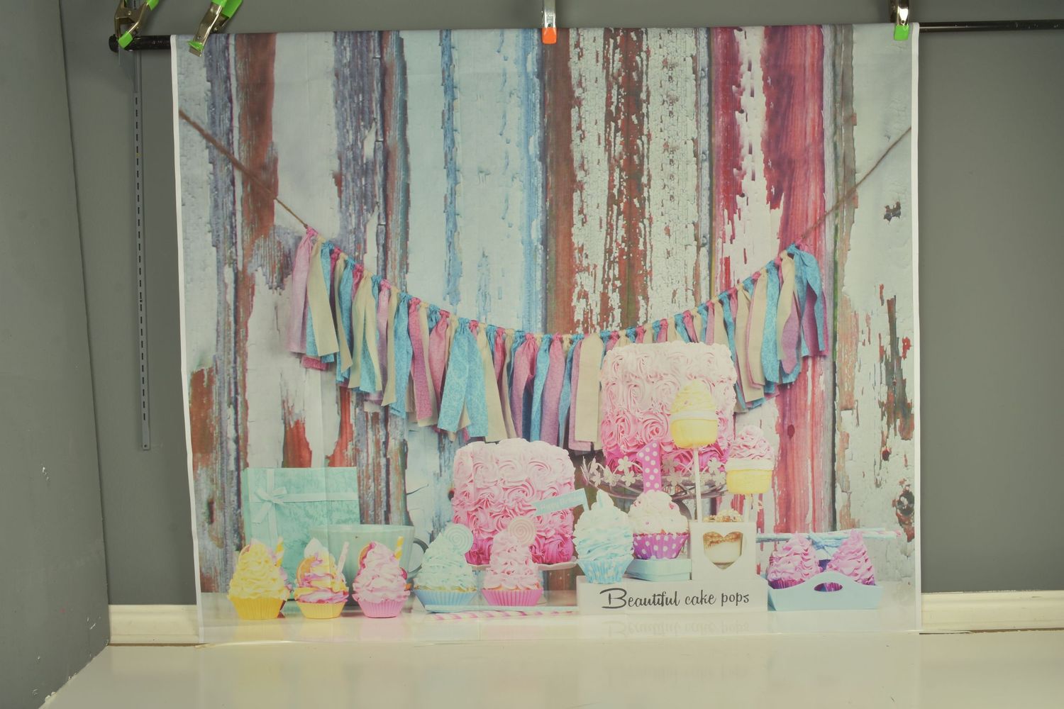 Pastel dessert table with pink cake, cupcakes, and colorful bunting against a rustic painted wood backdrop.