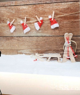 Miniature Santa hats hanging on a clothesline with wooden pegs, beside a toy sled and skis in snow.