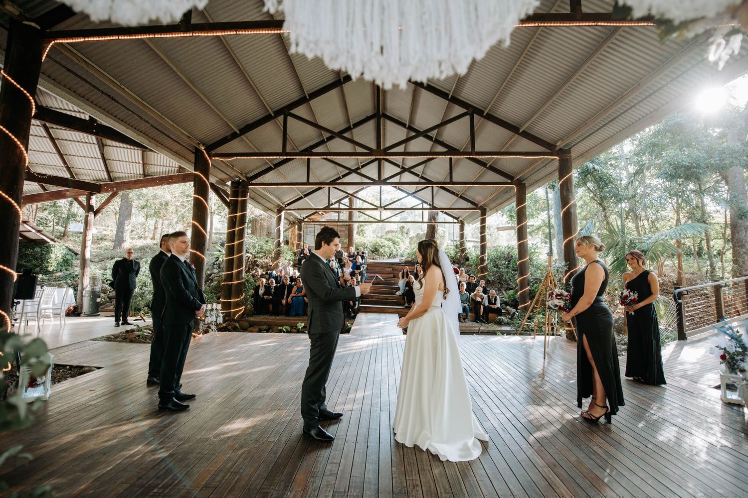 Wedding ceremony taking place on covered wooden deck surrounded by forest.