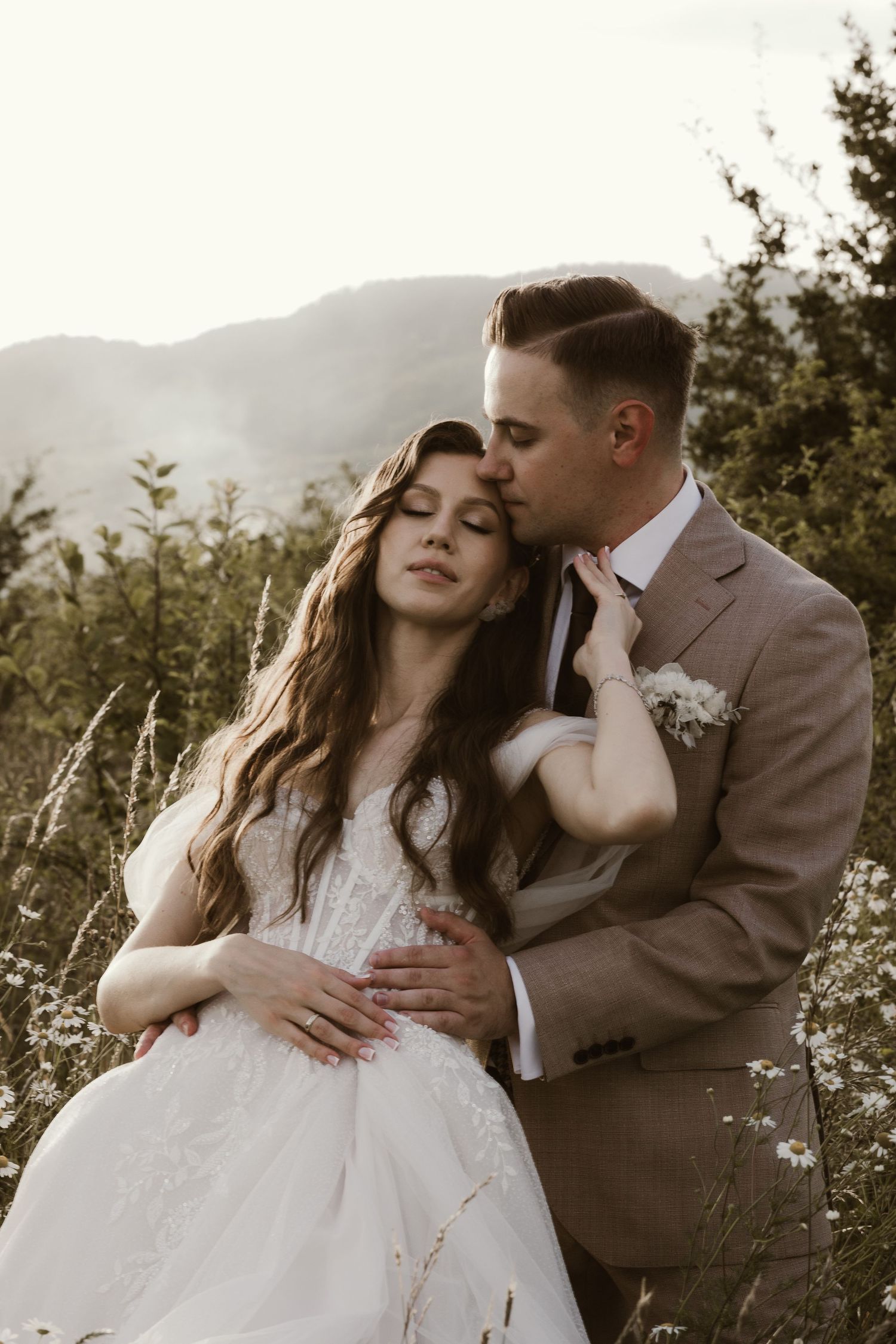A tender moment between newlyweds against a mountainous backdrop at sunset.
