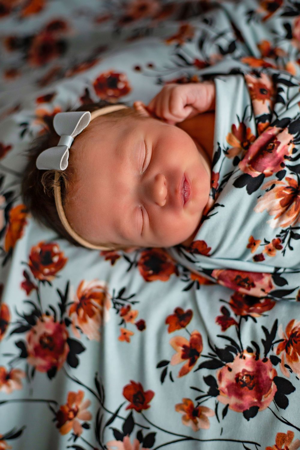 Sleeping baby lies on floral print fabric wearing white bow headband.