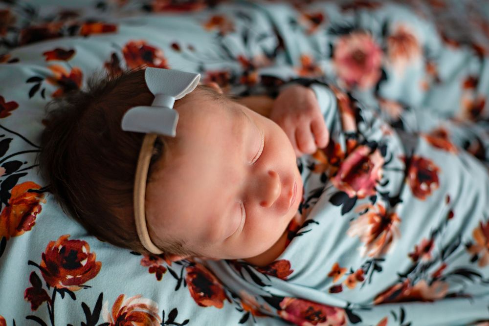 Close up of peaceful sleeping infant on blue and coral floral fabric with white bow.
