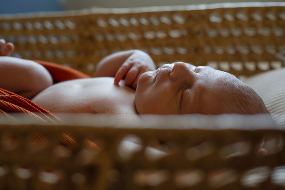 Peaceful sleeping baby in woven bassinet with orange wrap.
