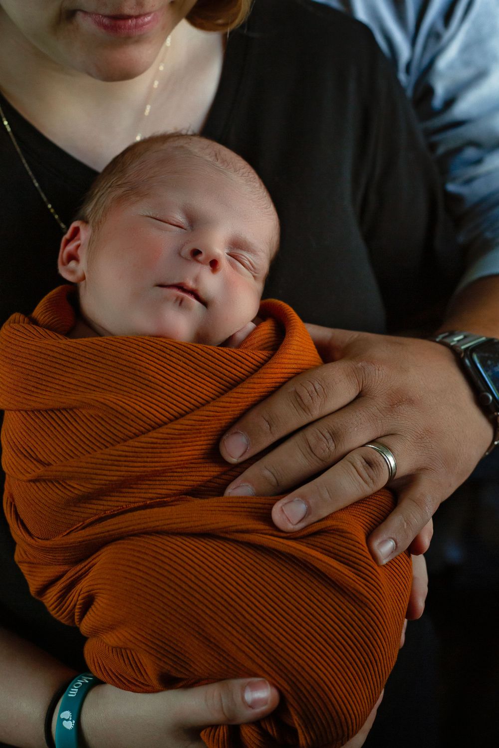 Sleeping baby in orange wrap being held securely with gentle hands.