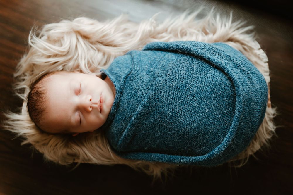 Sleeping infant peacefully wrapped in teal blanket resting on soft furry rug.