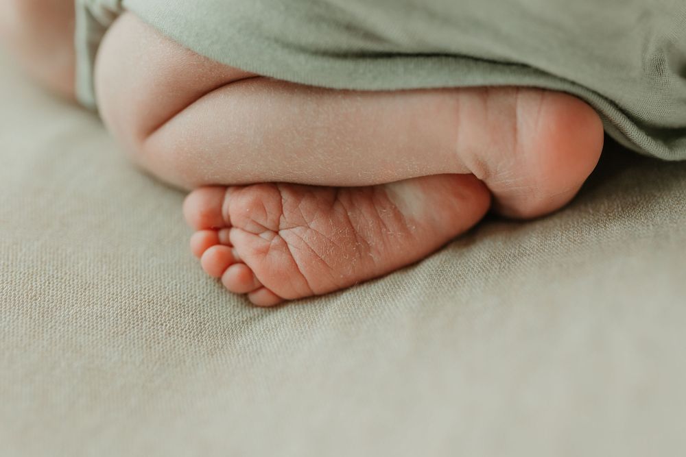 Close-up of a newborn baby's tiny feet resting on a soft beige blanket, partially covered by a green wrap.