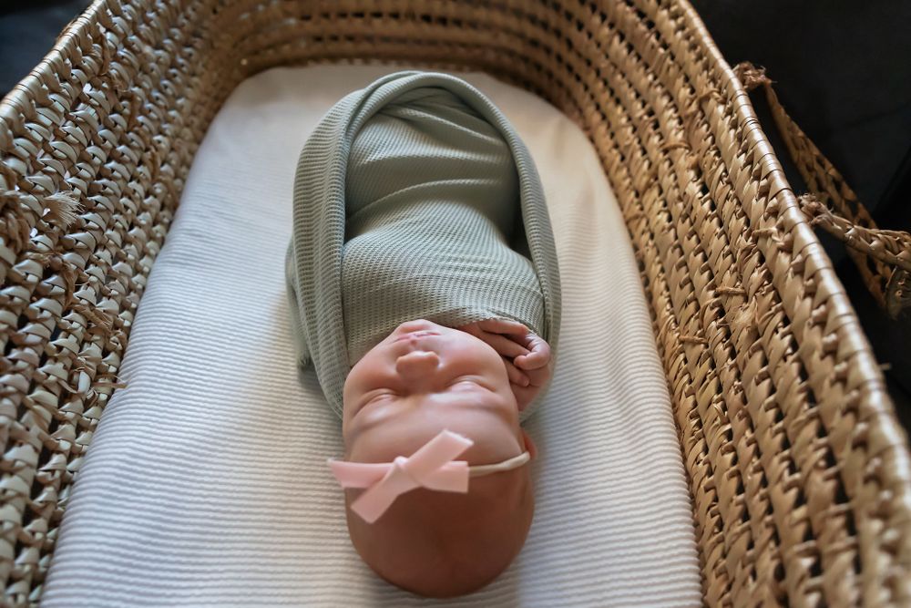 Newborn baby sleeping peacefully in woven bassinet with white bedding.