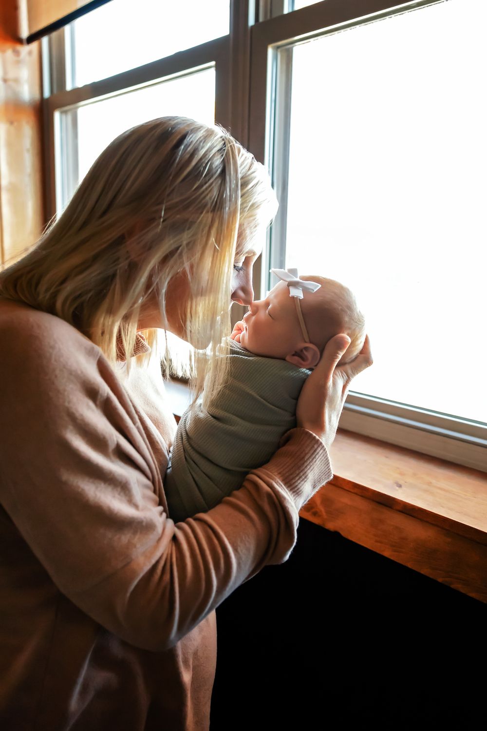 Tender moment between mother and newborn by sunlit window.