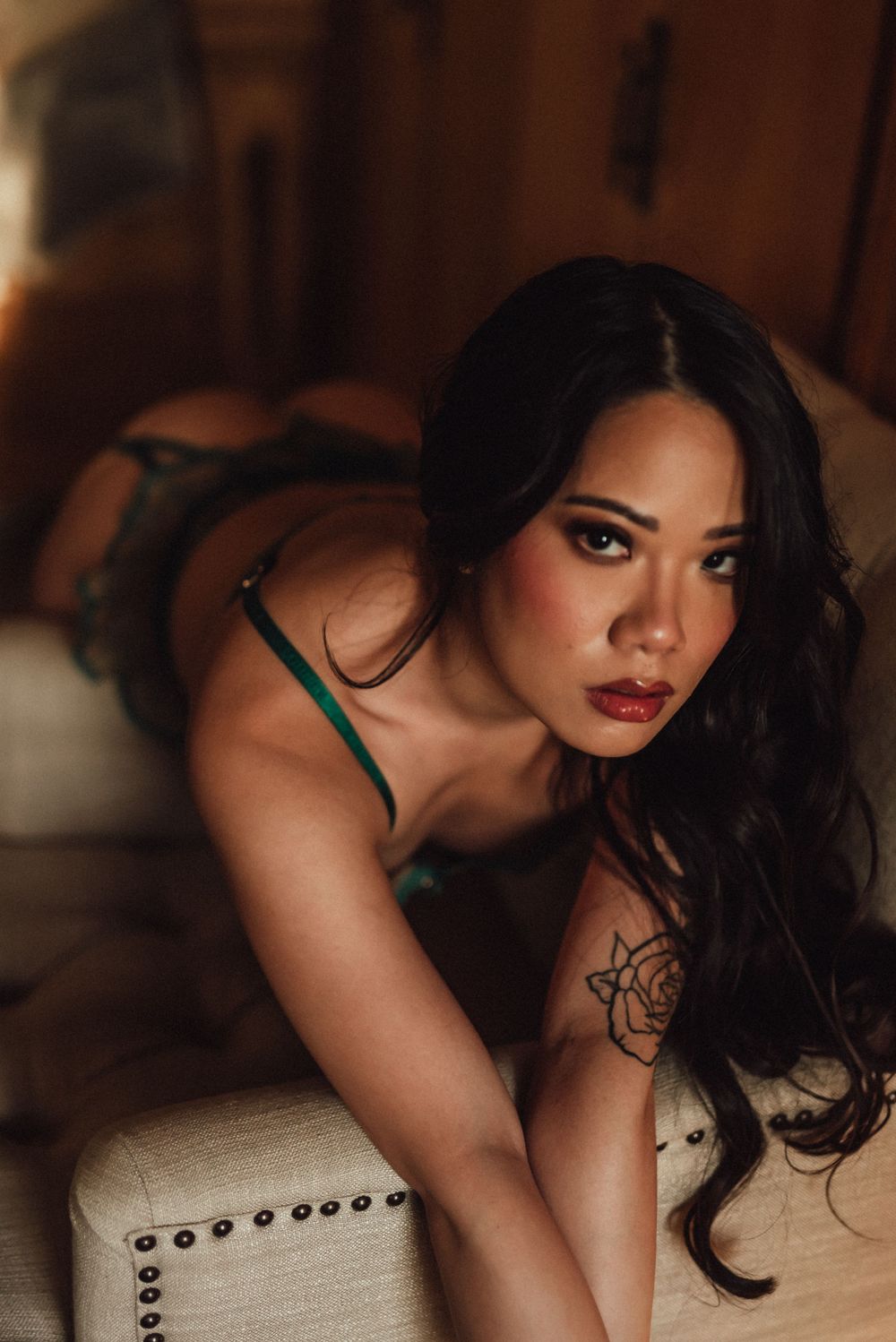 Artistic boudoir photo in warm lighting featuring a floral tattoo and long dark wavy hair.