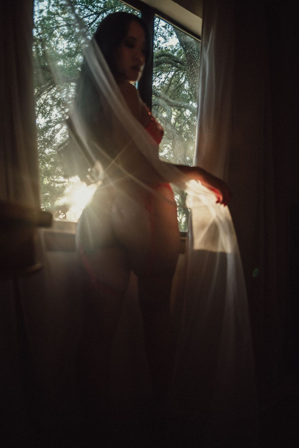 A figure in white fabric stands silhouetted against a sunlit window, creating an ethereal and dreamy atmosphere.