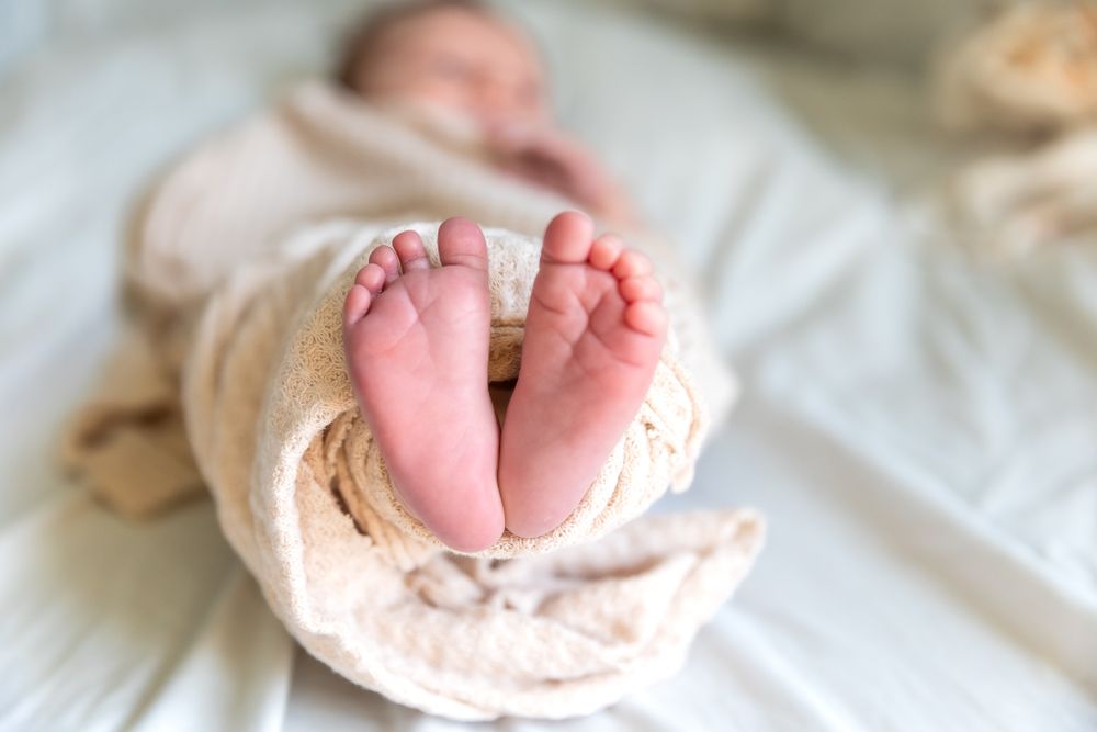 Close-up view of tiny newborn baby feet wrapped in a cream-colored blanket.