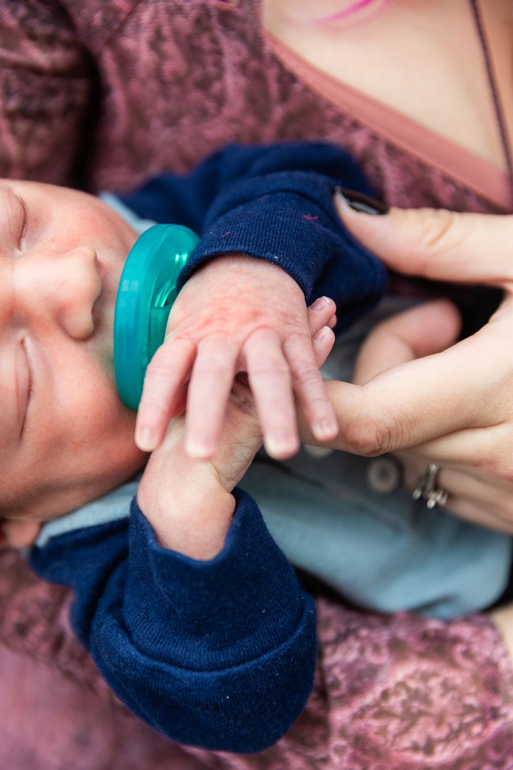 Close-up of baby's tiny hand grasping adult finger while wearing navy blue outfit.