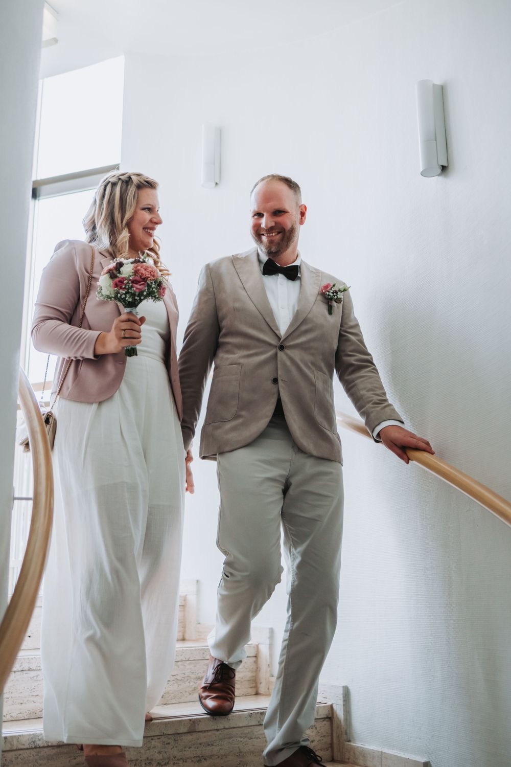 A couple descending white stairs together during their wedding.