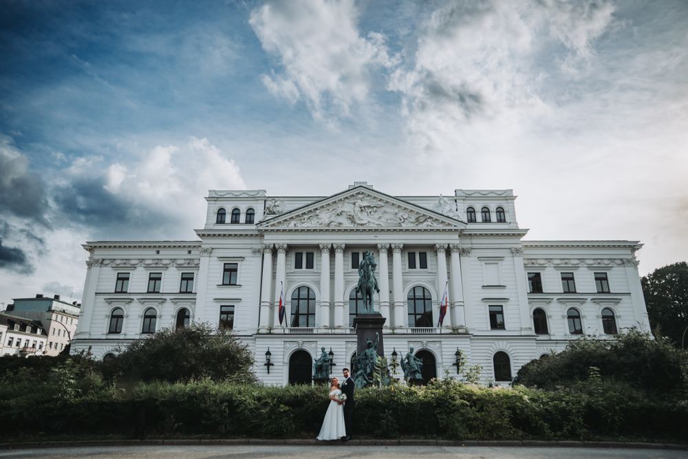 Grand white neoclassical building with wedding couple standing at its base.