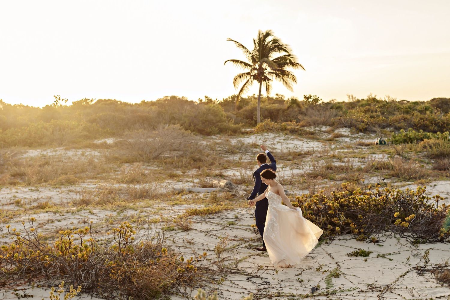 A beach wedding photo at sunset with palm trees and flowing dress creating a dreamy silhouette.