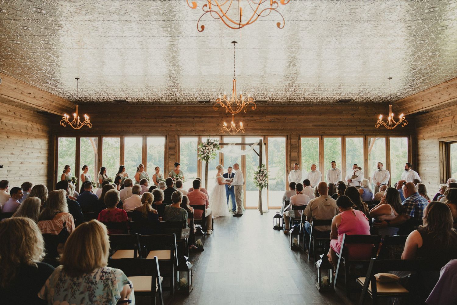 Indoor wedding ceremony in an elegant venue with chandeliers and large windows.
