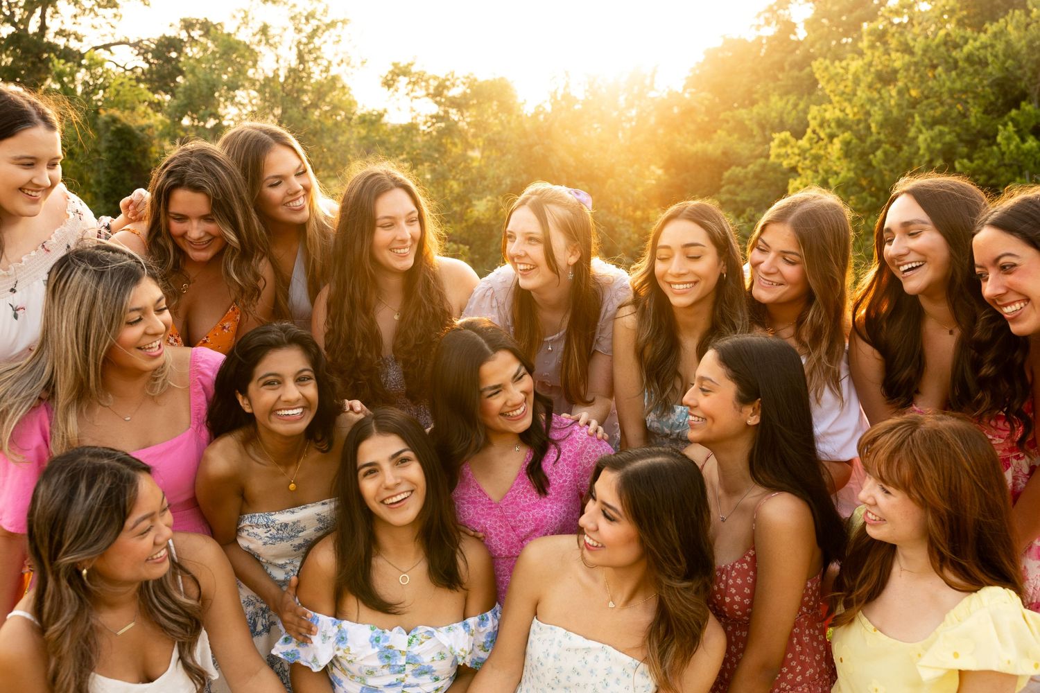 A joyful group wearing pink and white dresses poses together at sunset in a garden setting.