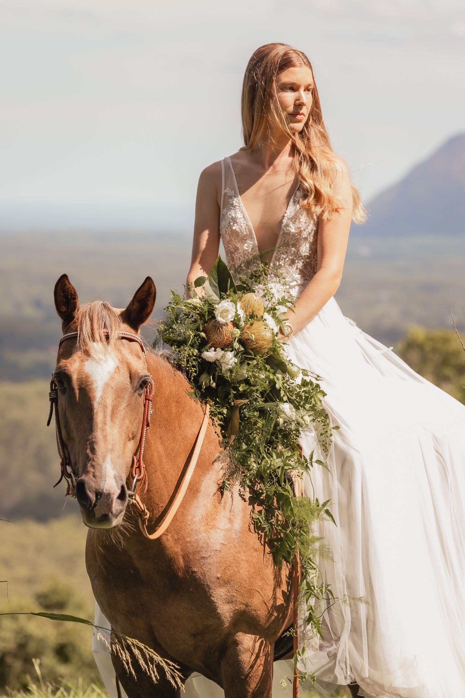 A white wedding dress against a desert landscape backdrop with a brown horse.