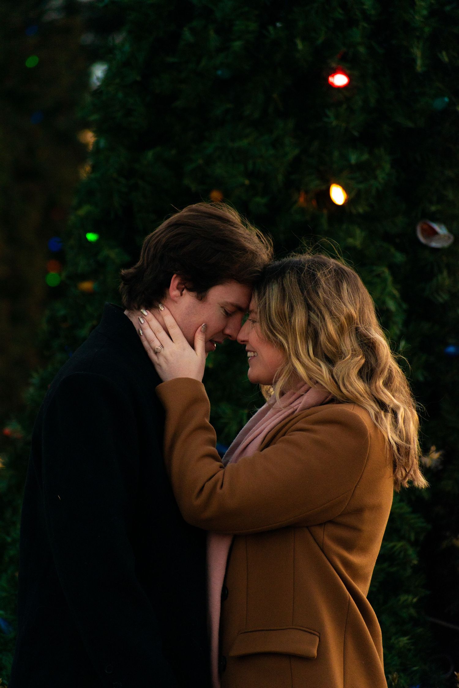 An intimate moment captured in front of a decorated holiday tree with colorful lights.