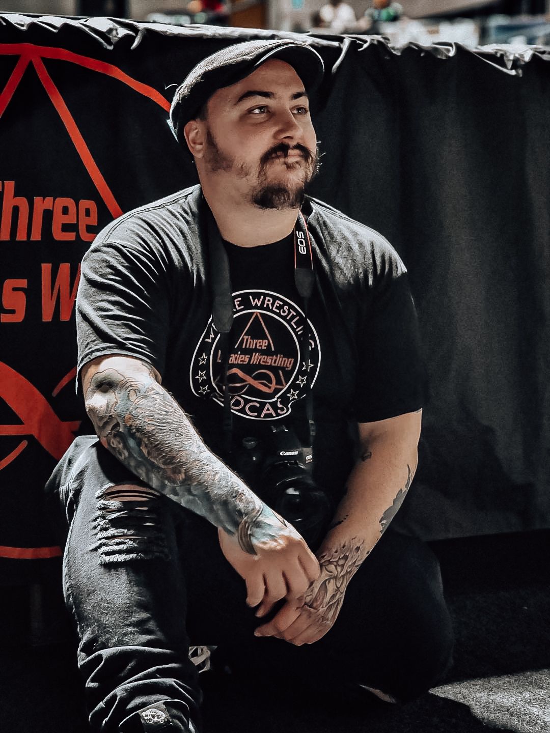 Portrait session featuring tattooed arms and black graphic t-shirt in dark studio setting.