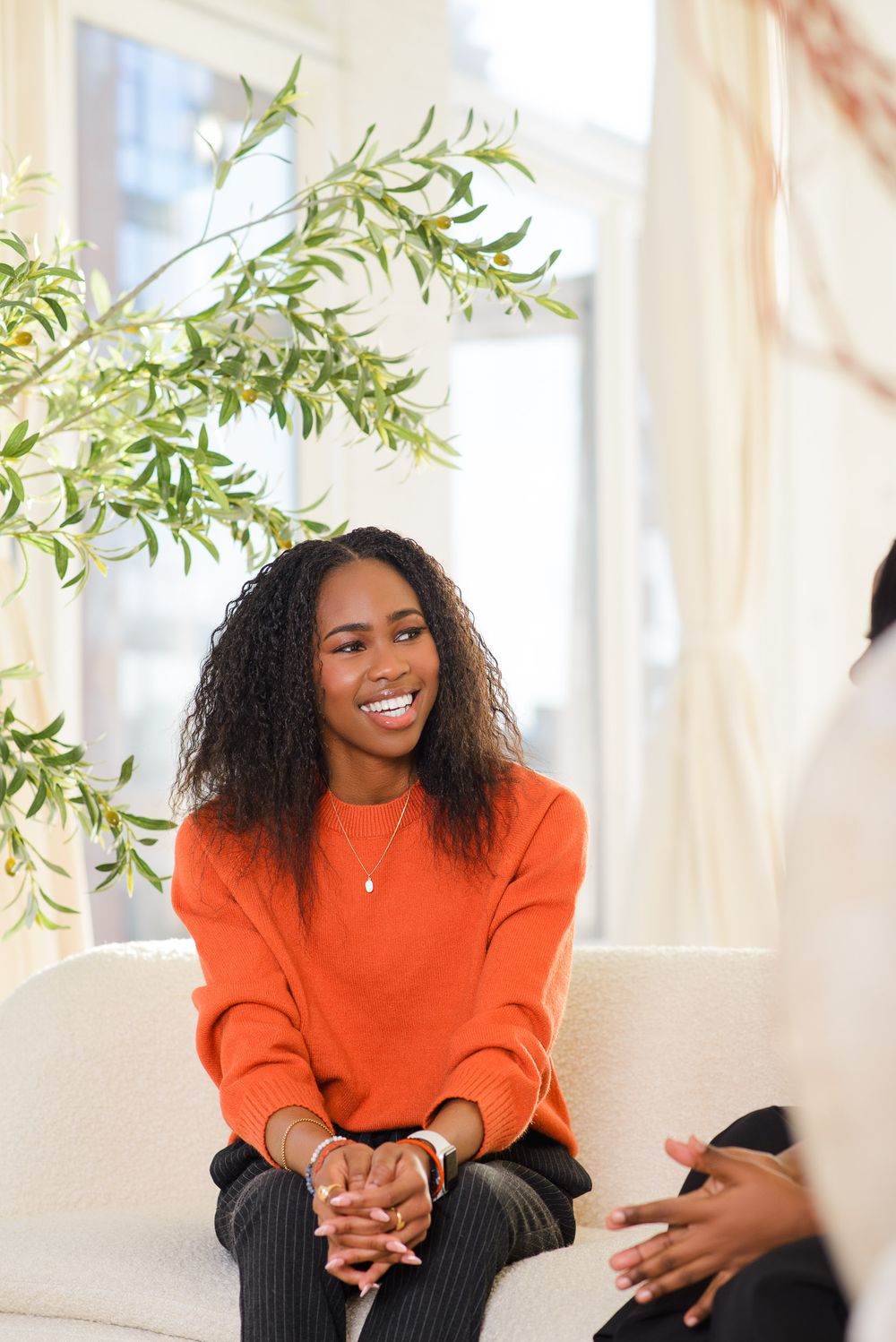 Person sitting on white couch near window with green plants.