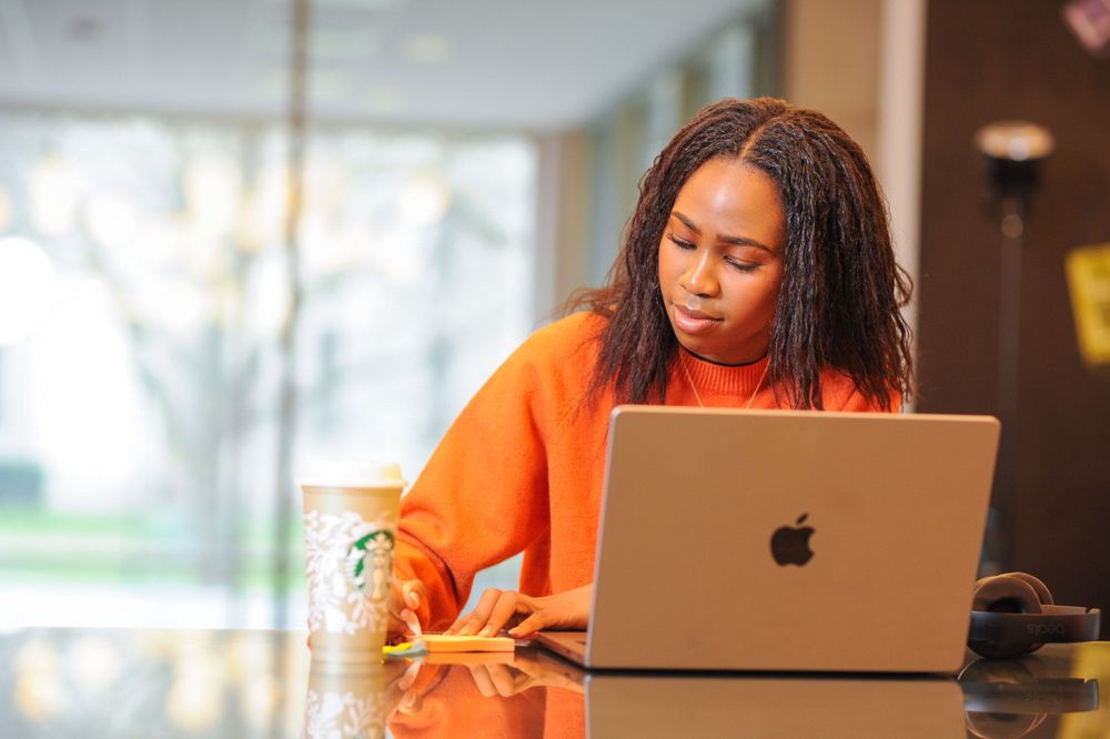 Person working on laptop in bright orange sweater.