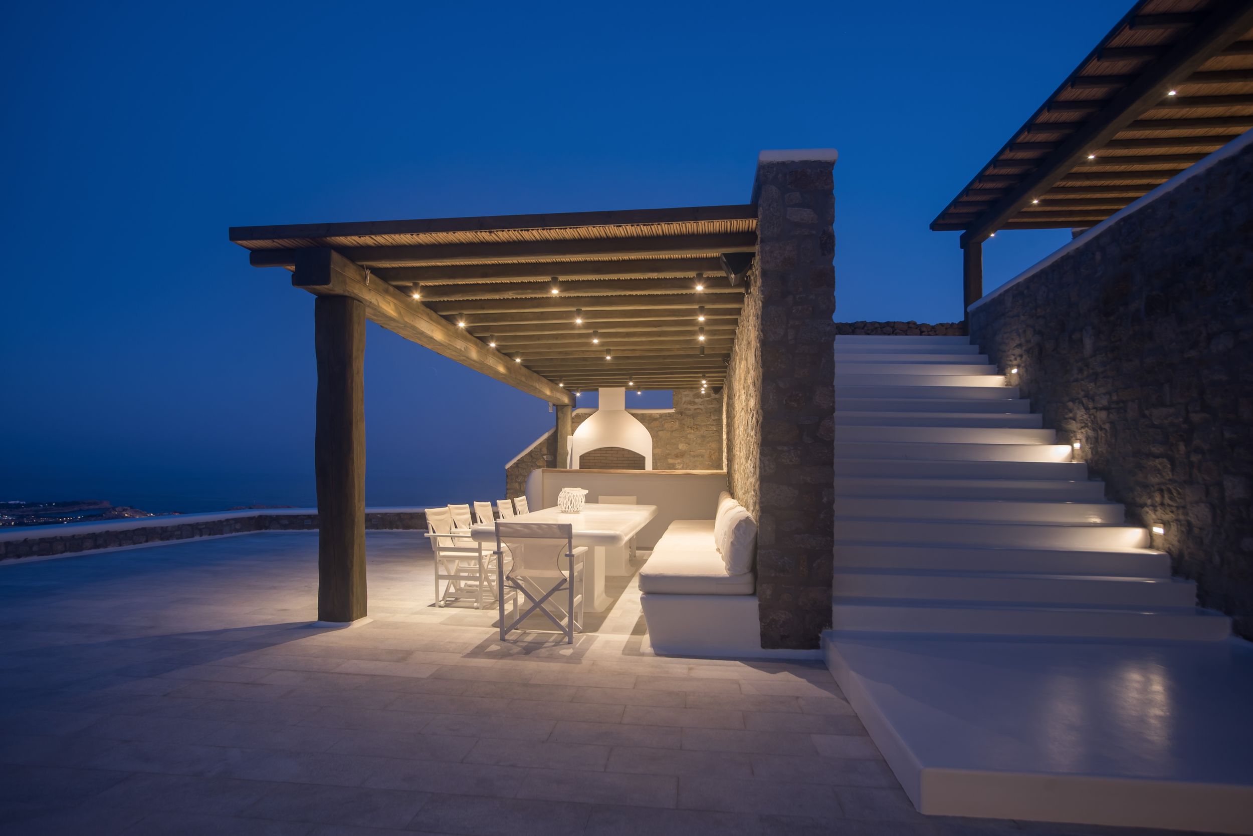Covered outdoor dining area with ocean views and modern lighting at dusk.