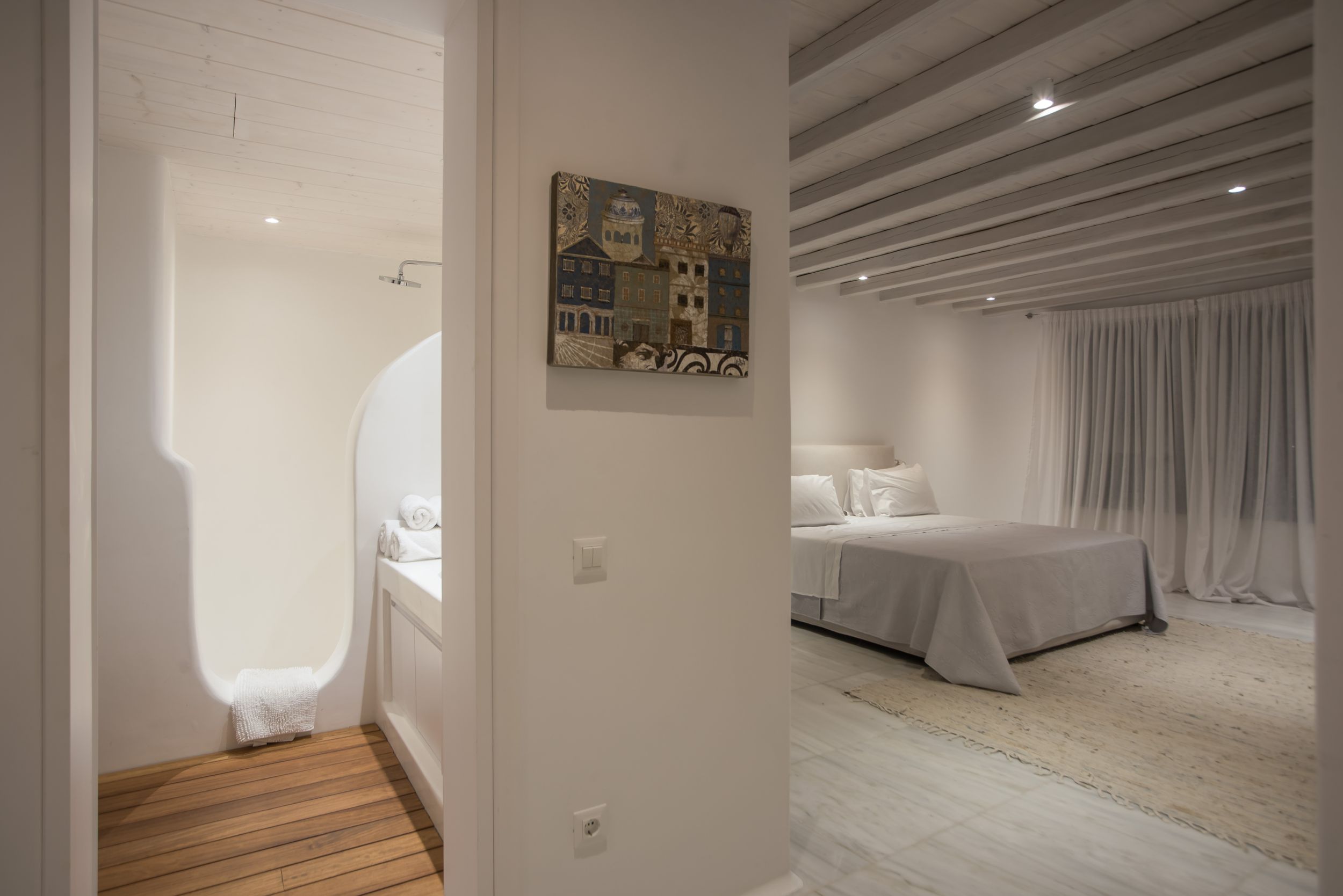 Modern minimalist white bedroom interior with wood floors, wall art, and flowing curtains in a luxury hotel setting.