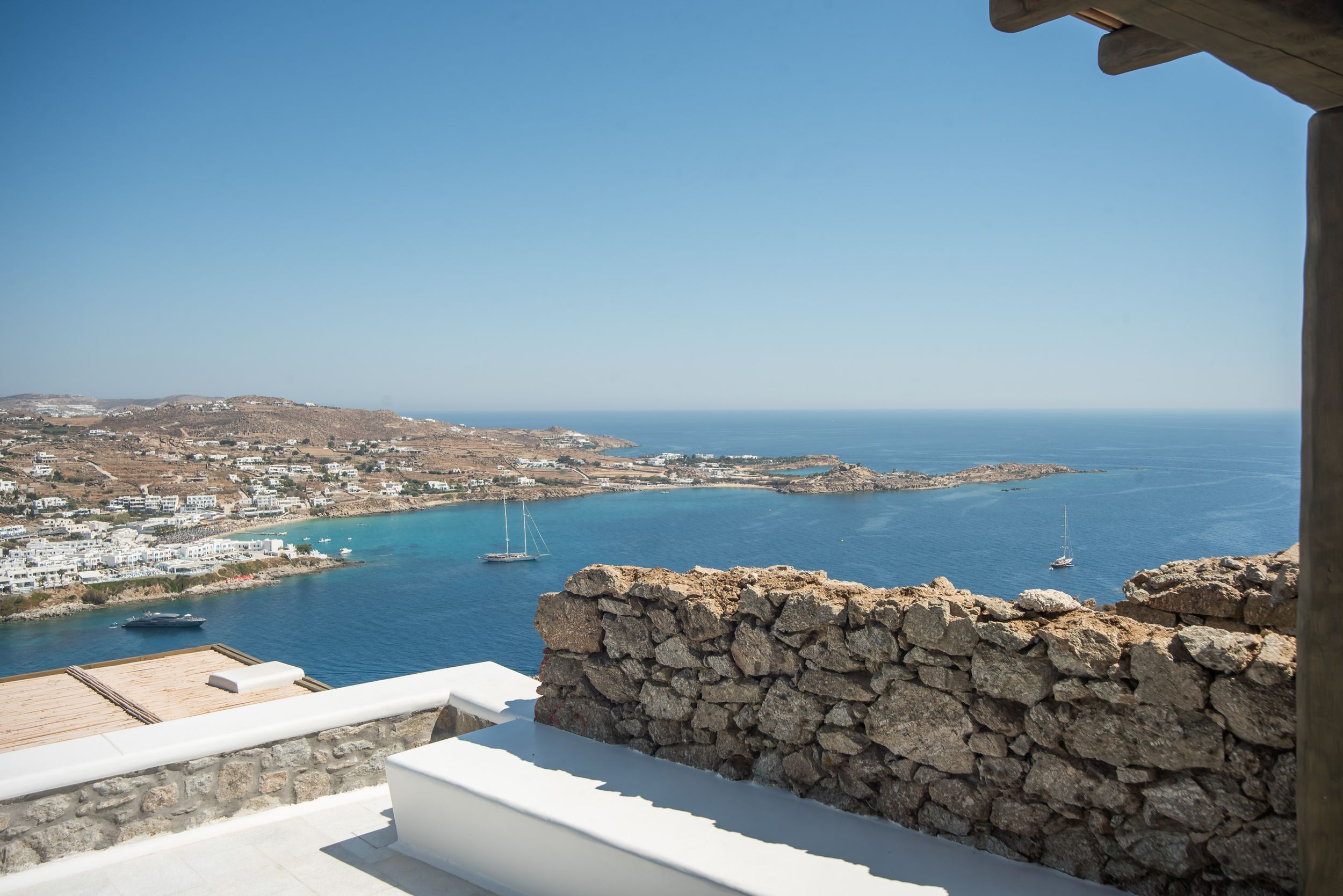 Scenic Mediterranean coastal view from stone terrace overlooking Mykonos harbor and blue sea on sunny day.